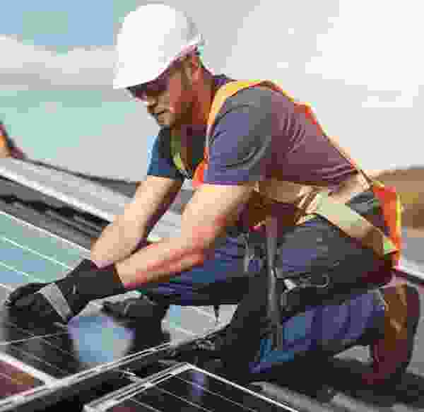 Technician wearing a hard hat and safety harness installing solar panels on a rooftop.