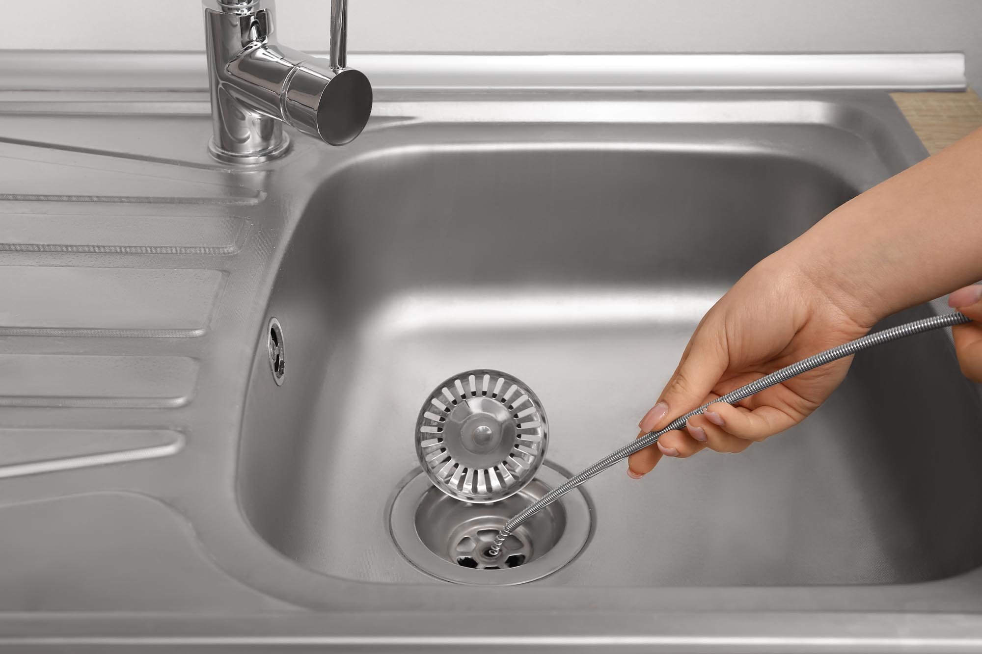 Woman cleaning drain with plumber's snake, closeup