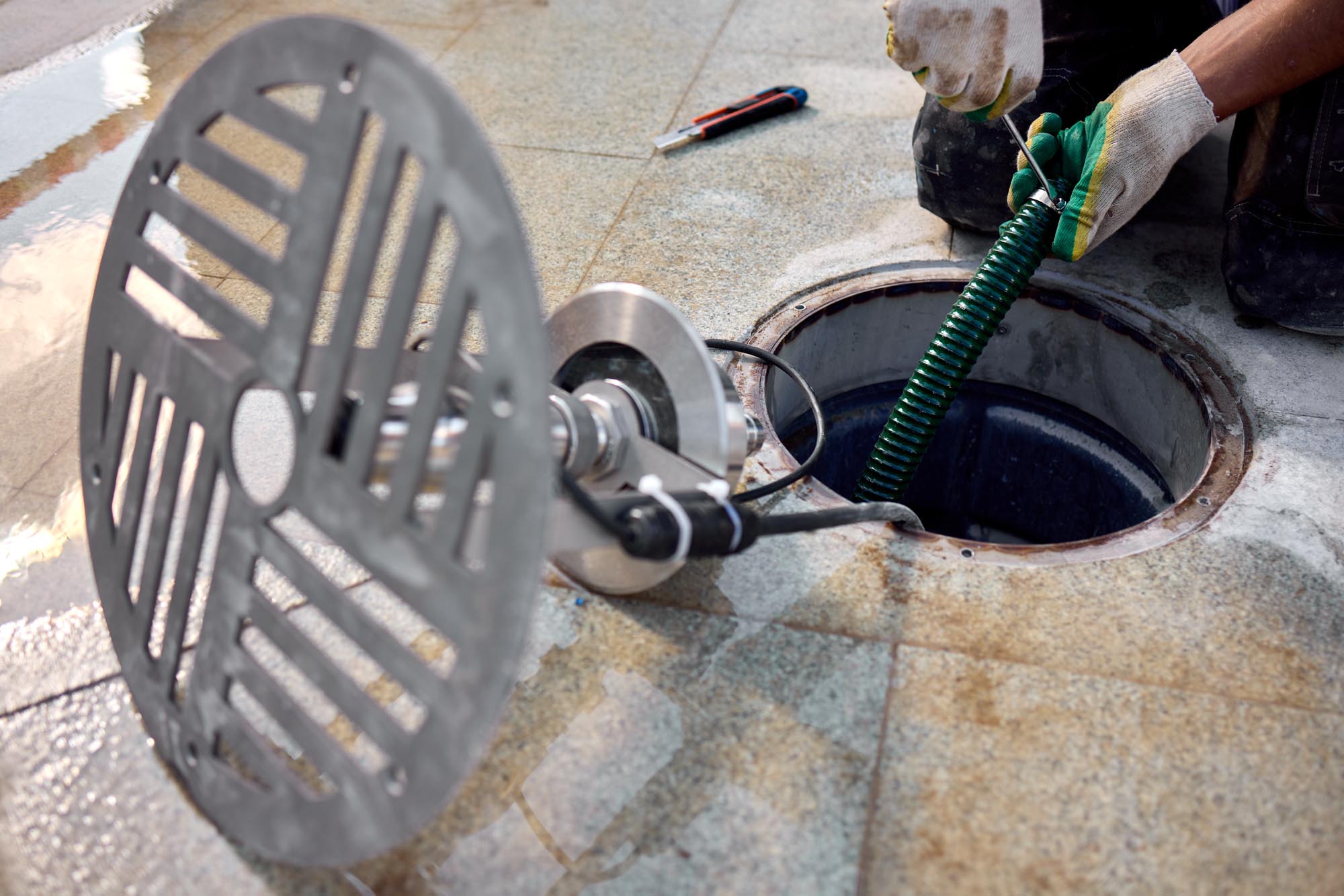 removal of manhole cover on sidewalk with concrete and metal materials, practical ground-level view, gray and green tones, utility maintenance in construction setting.