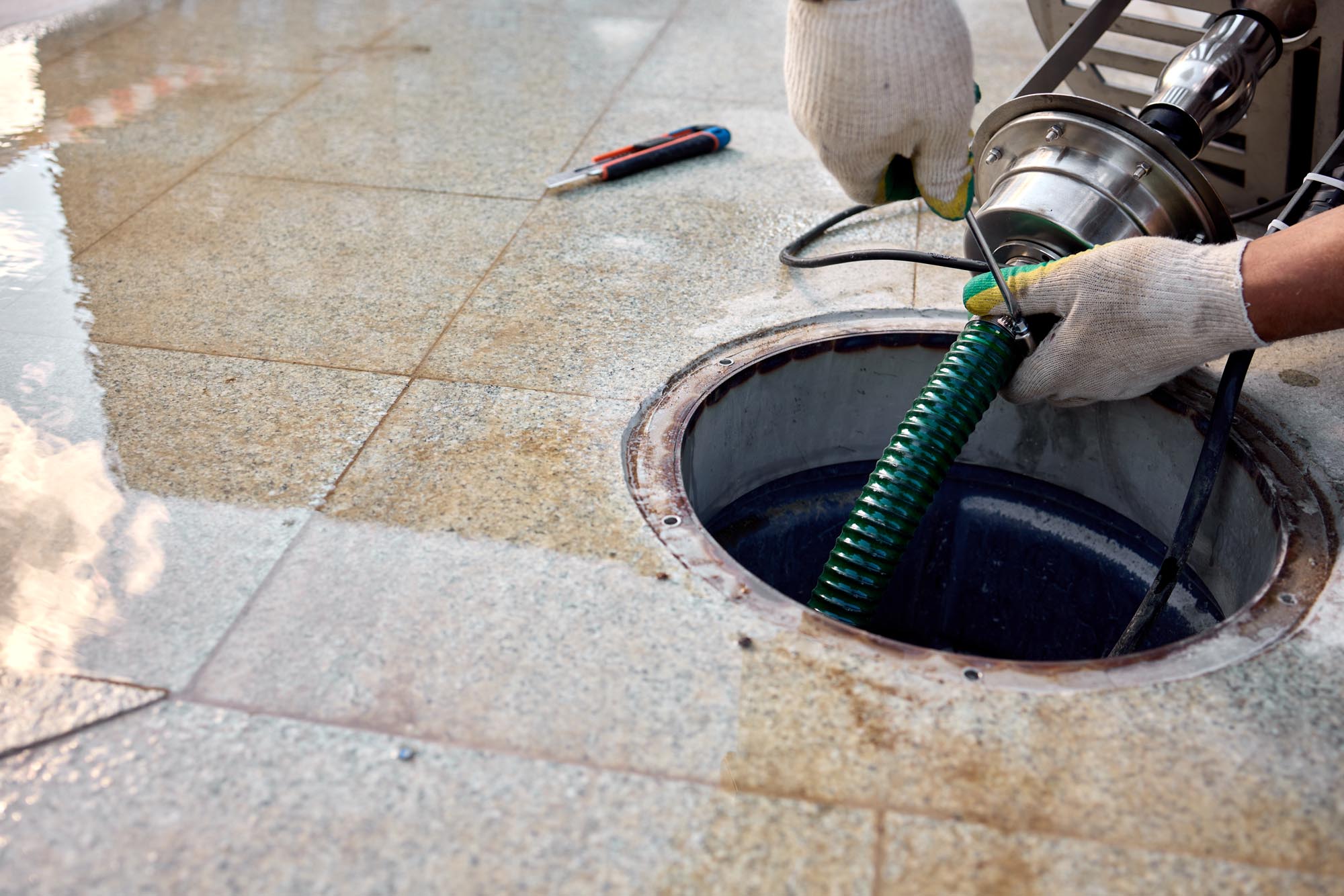 removal of manhole cover on sidewalk with concrete and metal materials, practical ground-level view, gray and green tones, utility maintenance in construction setting.