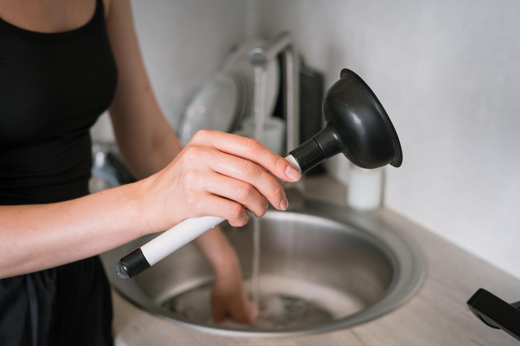 Woman using a plunger to unclog sink in modern kitchen