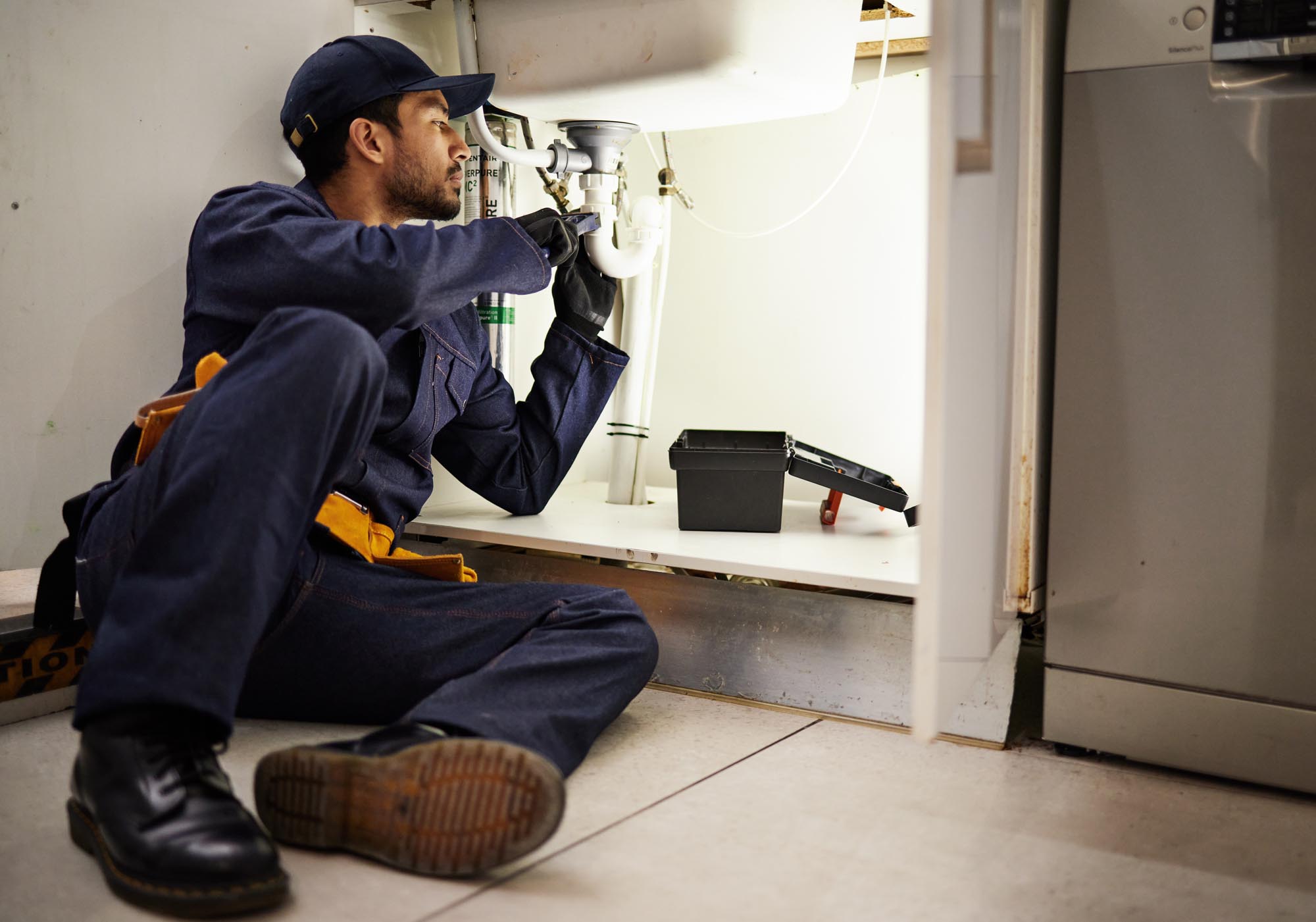 Plumbing, handyman and maintenance with man in kitchen for repair, industrial and inspection. Pipes, tools and safety with male plumber fixing sink for home improvement, drainage and water system