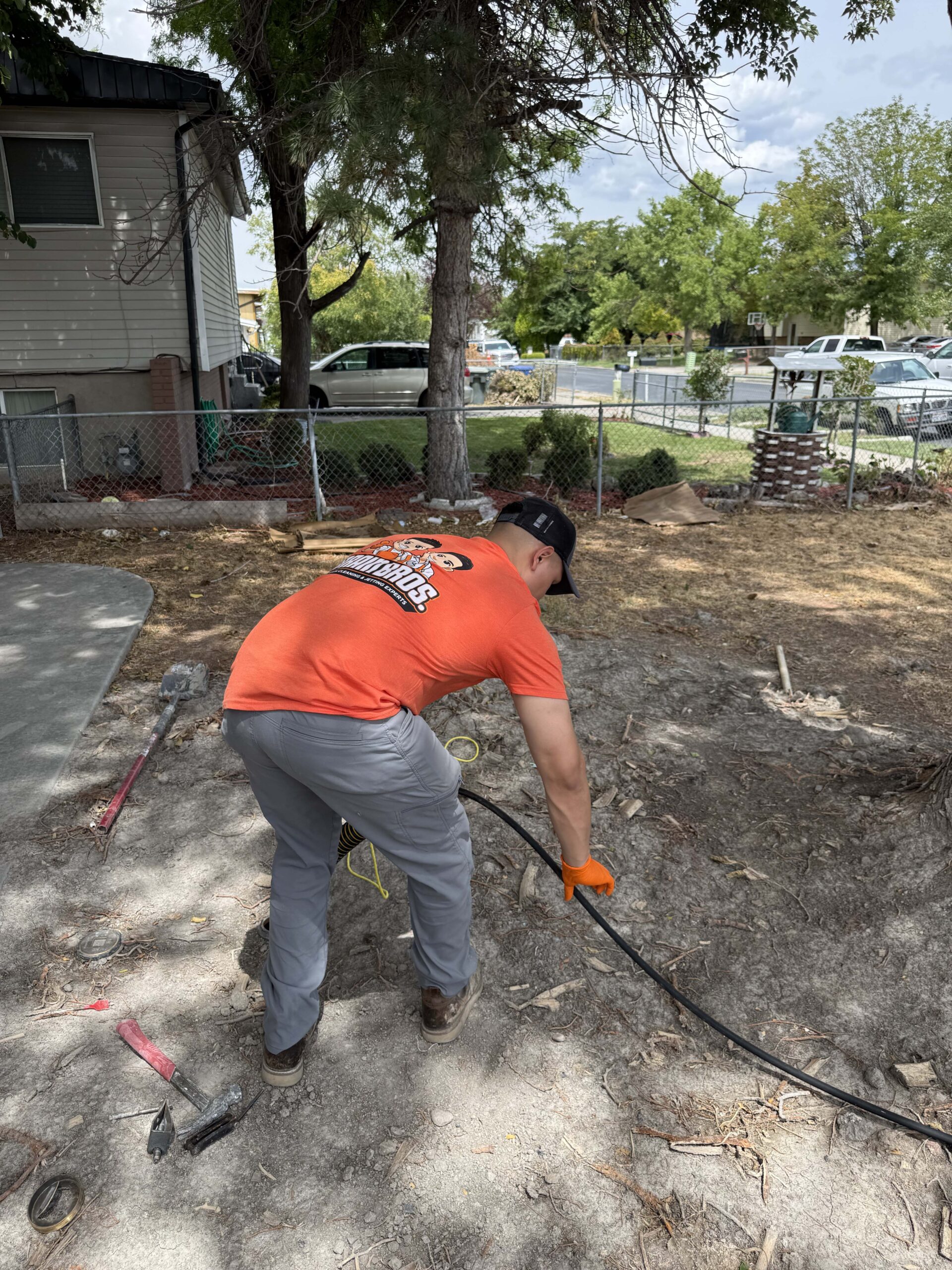 Drain Bros technician feeding a drain cable into an outdoor sewer line in a yard.