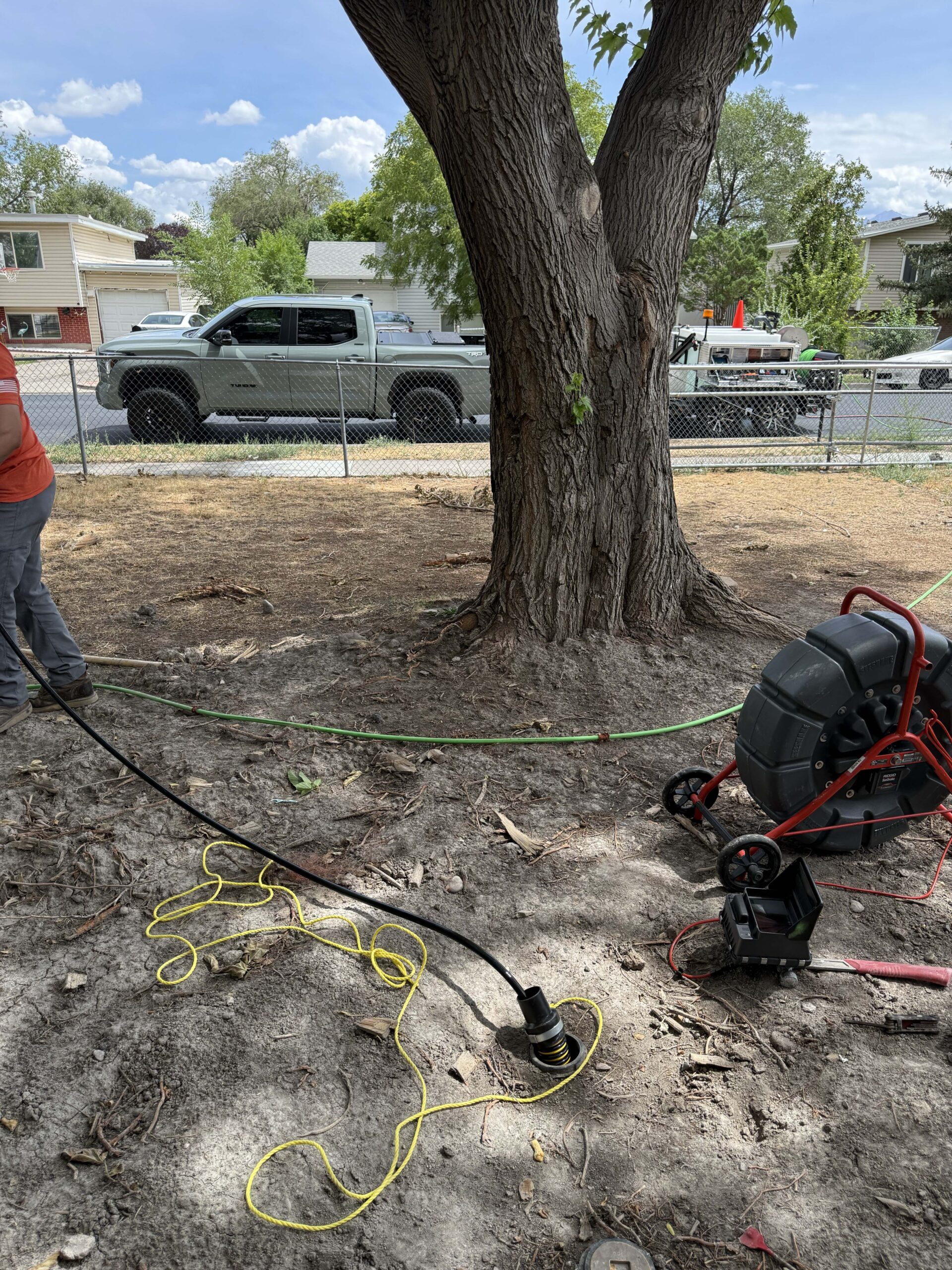 Sewer inspection camera cable inserted into an outdoor drain line next to inspection equipment in a residential yard.