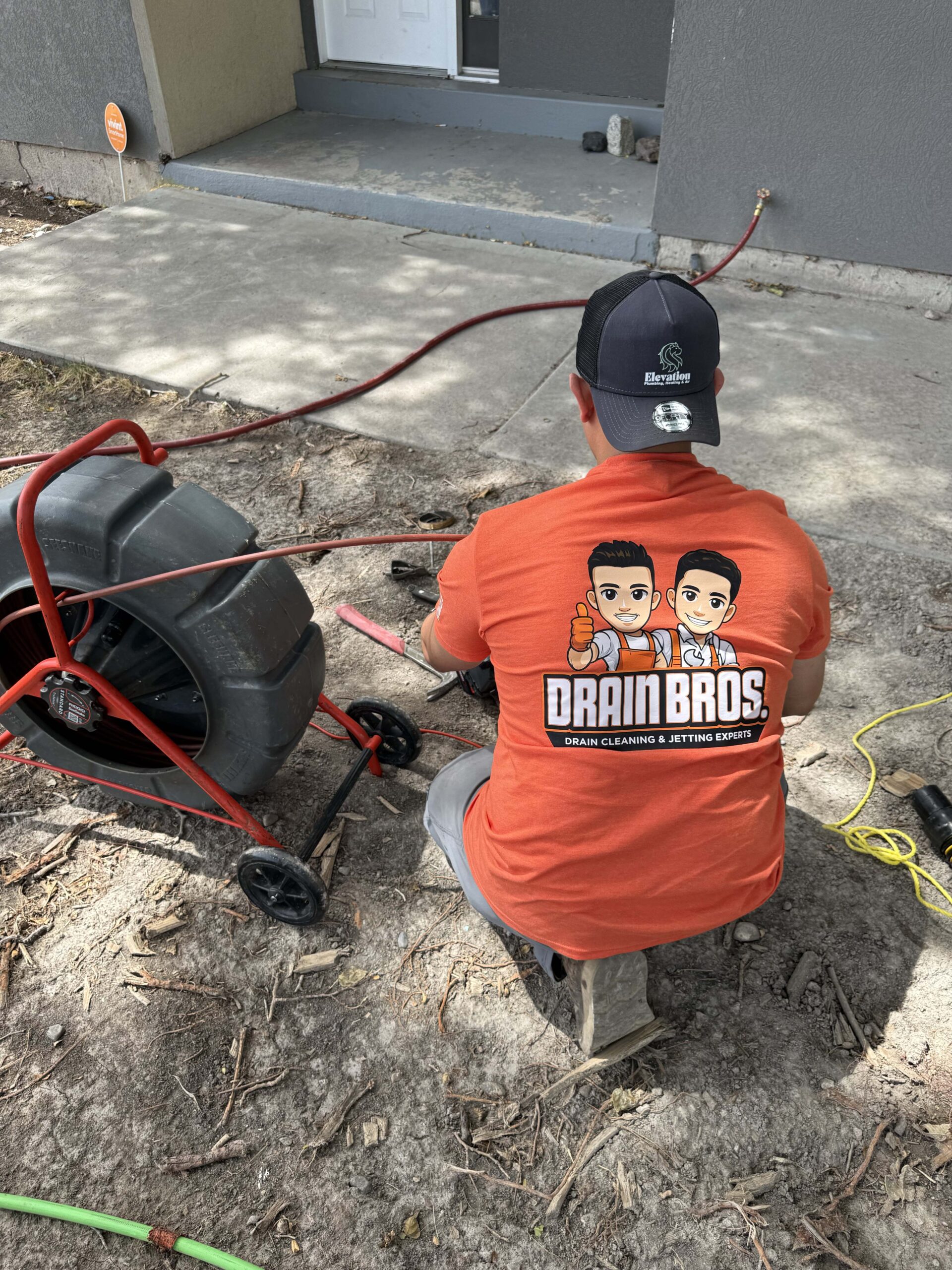 Drain Bros technician sitting on a step while managing sewer camera inspection cables outside a home.