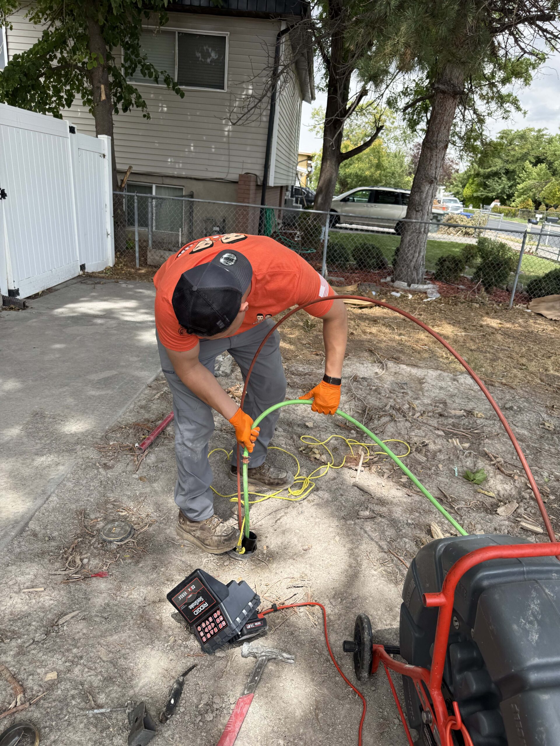 Drain Bros technician guiding a sewer camera inspection hose into an outdoor access pipe in a yard.